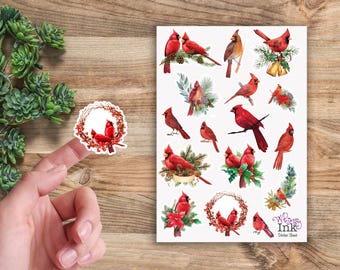 Pode incluir: Uma folha de autocolantes com várias ilustrações em aguarela de pássaros cardeais vermelhos pousados em ramos de pinheiro, azevinho e coroas. A folha inclui o texto Whimsy Ink Sticker Sheet no canto inferior direito, com um autocolante individual de coroa de cardeal mostrado separadamente.