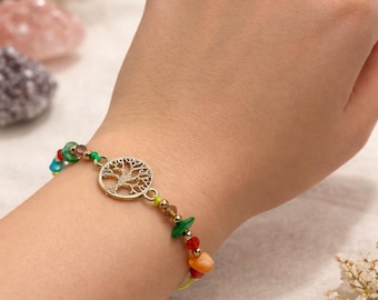 May include: A gold-colored bracelet featuring a tree of life charm and colorful gemstone beads. The bracelet is worn on a wrist, showcasing the design and the vibrant colors of the beads. The bracelet is a piece of jewelry.