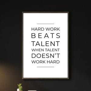 May include: Framed wall art with the quote "HARD WORK BEATS TALENT WHEN TALENT DOESN'T WORK HARD" in black text on a white background. The frame is dark brown, and the background is black.