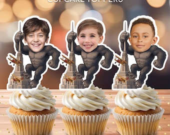 Op de afbeelding: Gepersonaliseerde cupcake toppers met drie kindergezichten op gorilla-lichamen, die het Empire State Building vasthouden. De toppers staan op cupcakes met witte glazuur. De tekst "Personalized CUPCAKE TOPPERS" staat bovenaan.