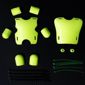Può includere: Una collezione di componenti di equipaggiamento protettivo verde neon, tra cui pettorali, protezioni per le braccia e ginocchiere, insieme a fascette verdi e nere. Gli oggetti sono disposti su una superficie scura, suggerendo un focus sulla sicurezza o sull'attrezzatura.