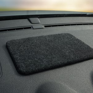 May include: A rectangular, dark gray DashMate dashboard mat sits on a black car dashboard. The mat has a textured surface and is designed to hold items in place. The DashMate logo is in the lower right corner.