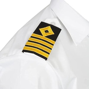 May include: A white dress shirt with a black and gold epaulette. The epaulette displays a gold diamond and three gold stripes on a black field. The shirt has a classic collar and a button.