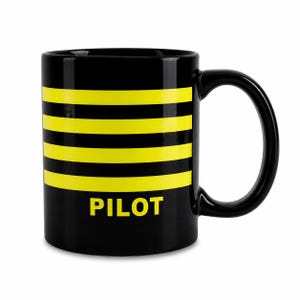 Peut inclure: Un mug en céramique noire orné de quatre bandes horizontales jaunes faisant le tour de l'extérieur. Le mot PILOT est imprimé en lettres capitales jaunes et grasses, centré sous les bandes. Le mug possède une anse incurvée sur le côté droit.