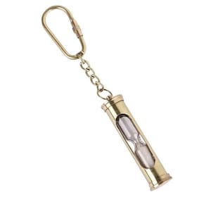 May include: A small, gold-colored hourglass keychain. The hourglass is encased in a cylindrical metal frame and connected to a chain and a clasp. The sand inside is visible, and the keychain is against a white background.