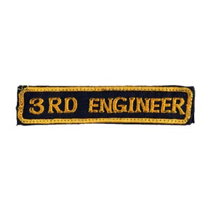 Op de afbeelding: Een rechthoekige marineblauwe patch met goud geborduurde tekst "3RD ENGINEER". De patch heeft een gouden rand en is waarschijnlijk voor een uniform of kledingstuk.
