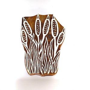 Puede incluir: Un bloque de impresión de madera con un diseño de espadañas blancas sobre un fondo marrón.