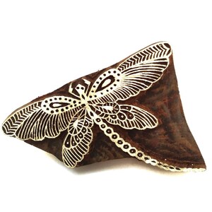 May include: A brown wooden block with a white detailed design of a butterfly. The block is used for printing patterns onto fabric.