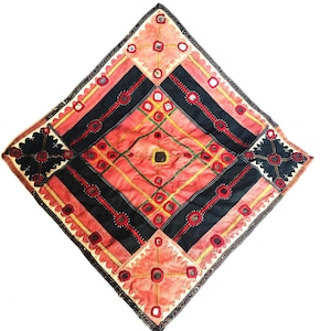 Puede incluir: Textil cuadrado hecho a mano con un patrón de diamantes. El diseño presenta secciones alternas en negro y coral, adornadas con costuras rojas, amarillas y verdes, y pequeños espejos reflectantes. Los bordes están acabados con un borde decorativo.