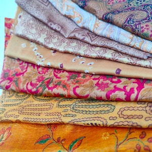 May include: A stack of colourful fabric scraps with floral and geometric patterns. The fabrics are in shades of brown, orange, pink, and green.