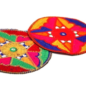 Puede incluir: Dos posavasos redondos de tela bordada de colores con intrincados patrones geométricos en tonos rojos, rosas, amarillos, verdes, azules y blancos.