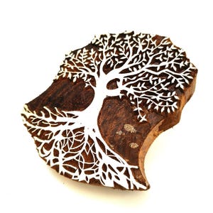 Puede incluir: Un bloque de madera tallado con un árbol con ramas y hojas intrincadas. La talla es blanca sobre un fondo de madera marrón.