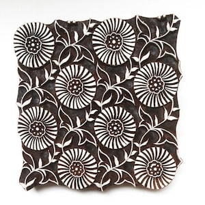 May include: A wooden printing block with a repeating pattern of stylized flowers and leaves. The block is brown with white details.