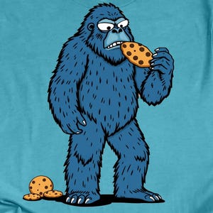 May include: A blue cartoon Bigfoot with a grumpy expression is eating a chocolate chip cookie. There are three more cookies on the ground.
