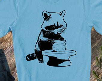 May include: A black and white illustration of a raccoon sitting on a pottery wheel, shaping a pot with its paws.
