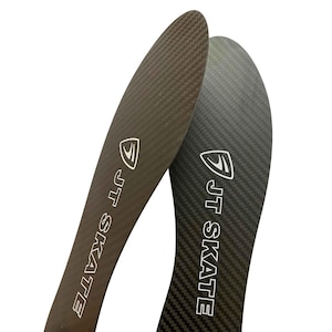 Puede incluir: Un par de plantillas de fibra de carbono negra con un patrón de textura tejida. Cada plantilla muestra un logotipo blanco que consiste en un icono de escudo estilizado sobre el texto JT SKATE impreso en una fuente sans-serif en negrita.