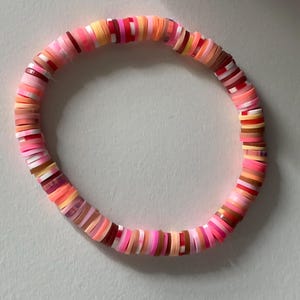 May include: A colorful bracelet made of pink, red, orange, and brown ceramic beads. The beads are stacked on top of each other to create a layered effect.