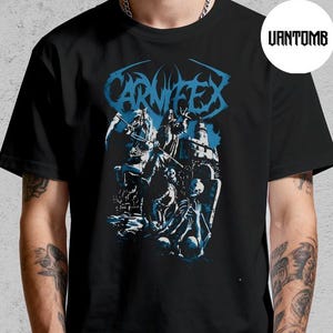 May include: Black t-shirt featuring the band name "CARNIFEX" in blue, above a detailed graphic. The graphic depicts figures in shades of blue and white. The shirt is a classic crew neck style.