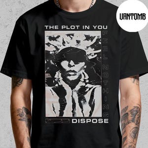 Puede incluir: Camiseta negra con un gráfico en blanco y negro de una persona. El texto "THE PLOT IN YOU" está encima de la imagen y "NOTHING DISPOSE" debajo. La camiseta la lleva una persona.