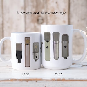 Puede incluir: Tazas de cerámica blanca con diseños de micrófonos vintage. Una taza está etiquetada como 11 oz, la otra como 15 oz. El texto "Microwave and Dishwasher safe" está impreso encima de las tazas. Las tazas tienen asas blancas.