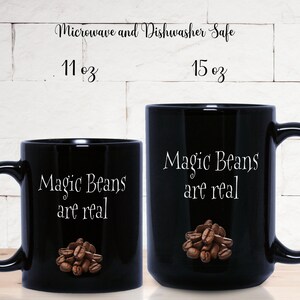 May include: Two black ceramic coffee mugs with white text that reads "Magic Beans are real". The larger mug is 15 oz and the smaller mug is 11 oz. Both mugs have a pile of coffee beans printed on them.