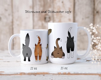 May include: Two white ceramic mugs with a design of cat butts. The smaller mug is 11 oz and the larger mug is 15 oz. Both mugs are microwave and dishwasher safe.