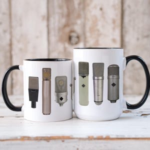 Puede incluir: Dos tazas de cerámica blanca con asas negras y bordes negros. Las tazas presentan un diseño de cinco micrófonos diferentes. Los micrófonos son todos plateados y negros con diferentes formas y tamaños.