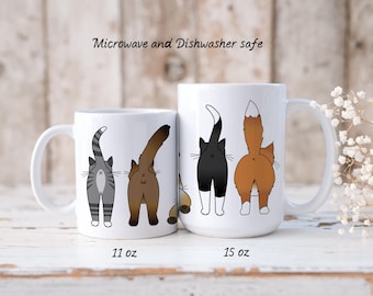 May include: Two white ceramic mugs with a design of four cat butts. The mugs are microwave and dishwasher safe. The smaller mug is 11 ounces and the larger mug is 15 ounces.