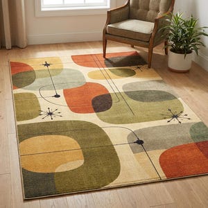 May include: A rectangular area rug with an abstract mid-century modern design. The rug features large, overlapping shapes in shades of orange, green, and beige, with black lines and starburst accents. The rug is placed on a hardwood floor.