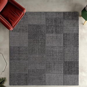 May include: A gray patchwork rug with a textured surface. The rug is made up of different squares of fabric, each with a slightly different pattern.