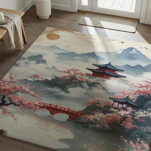 May include: A large area rug featuring a Japanese landscape scene. The design includes a red bridge, pagodas, cherry blossoms, and mountains. The color palette is soft, with shades of pink, red, blue, and cream.