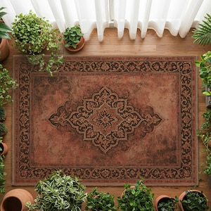 May include: A rectangular rug with a central medallion design in shades of brown and rust. The rug has a detailed border and is surrounded by potted plants, creating a warm atmosphere. The rug is placed on a wooden floor.