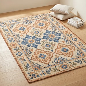 May include: A rectangular area rug with a cream-colored background and a repeating floral pattern in shades of blue, orange, and green. The rug has a border with similar floral motifs. The rug is placed on a wooden floor.