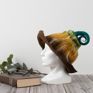May include: A brown, yellow, and green felt hat with a curled green felt brim. The hat is sitting on a white mannequin head.