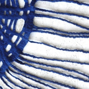 May include: Abstract textile art piece featuring a vibrant blue, textured fabric with a cut-out design. The blue fabric is set against a white, textured background, creating a striking contrast. The design includes both linear and circular cut-outs.