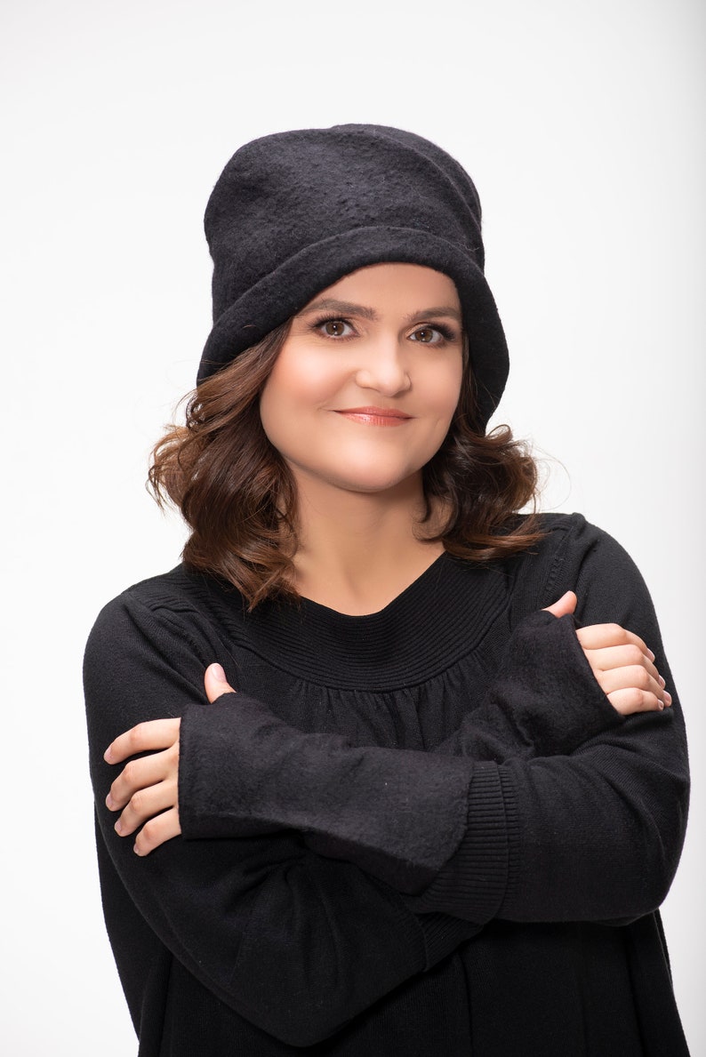 May include: A woman with brown hair wearing a black beanie and a black sweater with her arms crossed.