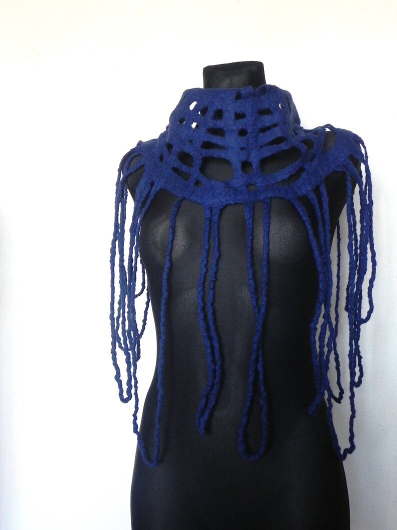 May include: A dark blue felted wool neck piece with a unique design. The top portion features a series of cut-out shapes, while long, dangling strands hang down. The neck piece is displayed on a black mannequin against a white background.