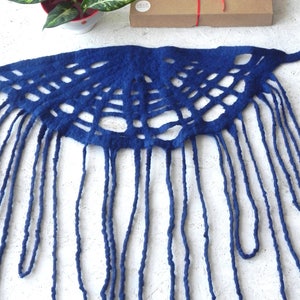 May include: A deep blue, handmade felt scarf with a unique openwork design and long fringe. The scarf is displayed on a white surface, with a small potted plant and a brown gift box tied with red ribbon in the background.