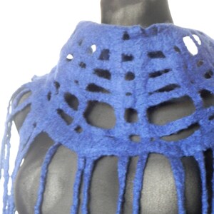 May include: A vibrant blue felt shawl with a unique openwork design. The shawl features a high collar and long fringe detailing, creating a textured and stylish accessory. The color is a deep, saturated blue.