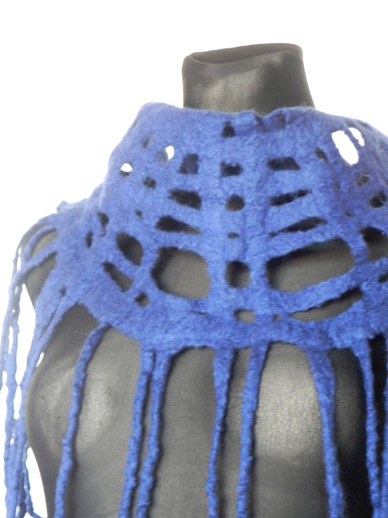May include: A vibrant blue felt shawl with a unique openwork design. The shawl features a high collar and long fringe detailing, creating a textured and stylish accessory. The color is a deep, saturated blue.