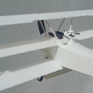 May include: A white model airplane with three sets of wings, a propeller, and a black tail. The model is made of plastic and has a detailed design.