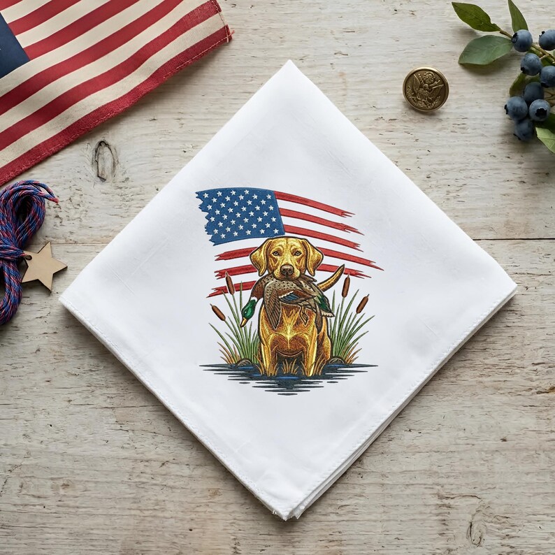 May include: White handkerchief featuring a yellow Labrador Retriever holding a duck, with an American flag design in the background. The dog is surrounded by reeds, creating a patriotic and outdoorsy theme.