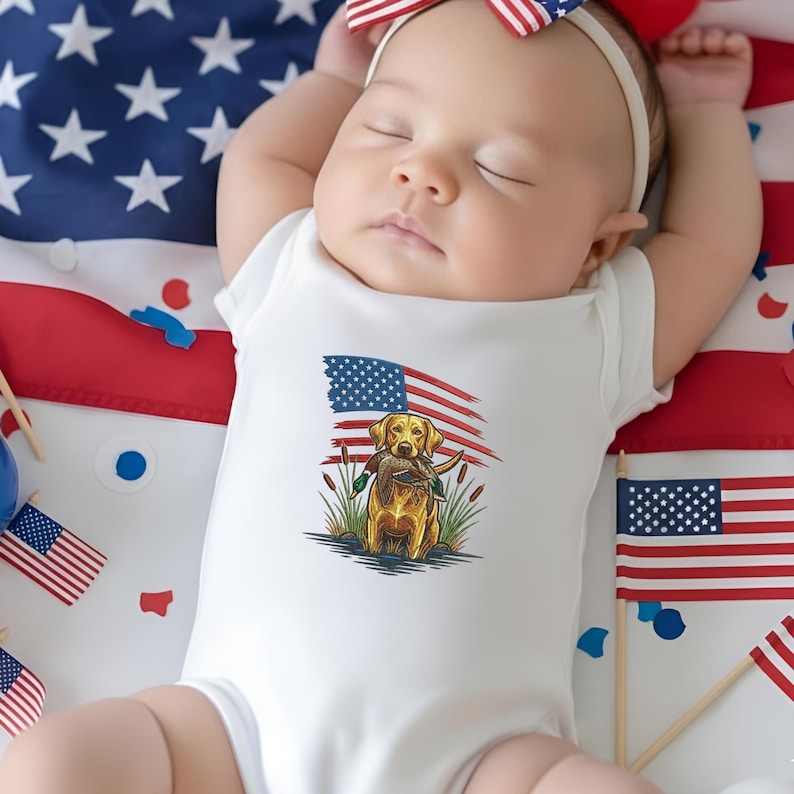 May include: A sleeping baby wearing a white onesie with a graphic of a golden retriever holding a duck in front of an American flag. The baby is lying on a surface decorated with the American flag and small flags.