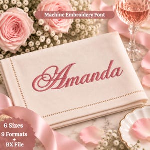 May include: A folded cream-coloured fabric napkin featuring the name Amanda embroidered in a dark pink script font. The text Machine Embroidery Font is visible at the top, and the text 6 Sizes 9 Formats + BX File is at the bottom left.