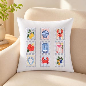 May include: A white square throw pillow featuring a grid of nine postage stamp-style illustrations. The designs include lemons, a seashell, a lobster, a hibiscus flower, a tin of sardines, a cocktail, an oyster, a crab, and olives on a branch.