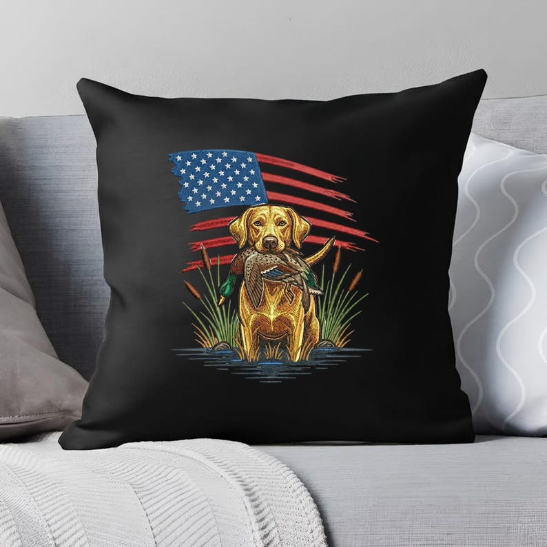 May include: Black throw pillow featuring a golden retriever holding a duck in its mouth, with an American flag design in the background. The dog is in water with reeds. A patriotic themed decorative pillow.