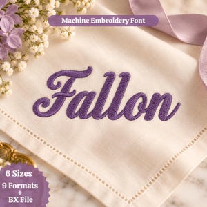 May include: A cream-colored fabric napkin featuring the purple machine-embroidered name Fallon in a cursive script. The text Machine Embroidery Font is visible at the top, and a purple ribbon and white flowers are present in the corners.