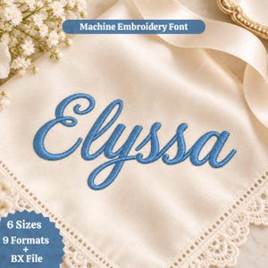 Op de afbeelding: Een crèmekleurig stoffen vierkant met een kanten rand met de blauwe machinaal geborduurde naam Elyssa in cursief schrift. De tekst Machine Embroidery Font, 6 Sizes, 9 Formats + BX File is zichtbaar op de stof en een blauwe sterbadge.