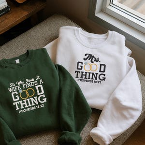 Könnte beinhalten: Zwei Sweatshirts, eines grün und eines weiß, werden gezeigt. Das grüne Sweatshirt trägt den Text "He Who Finds A Wife Finds A Good Thing Proverbs 18:22". Das weiße Sweatshirt trägt den Text "Mrs. Good Thing Proverbs 18:22".