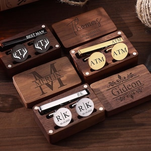 Può includere: Scatole regalo in legno con gemelli e fermacravatte personalizzati. Le scatole sono incise con nomi e iniziali. Alcuni gemelli sono neri con disegni bianchi, altri dorati. Il testo "BEST MAN", "Groomsmans" e "Gideon" è visibile.